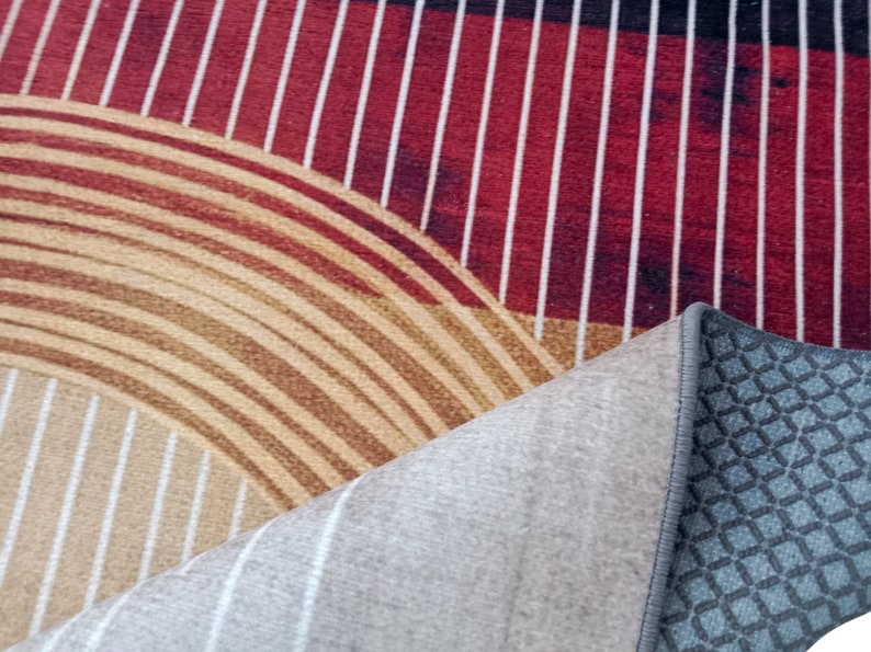 May include: Close-up of a rug with a geometric pattern of red and white stripes, brown and white concentric circles, and a gray backing with a diamond pattern.