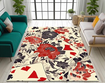 May include: A rectangular area rug with a floral and playing card design. The rug features large red and black flowers, with playing card suits, including hearts and clubs. The background is a cream color, and the rug is placed in a living room setting.