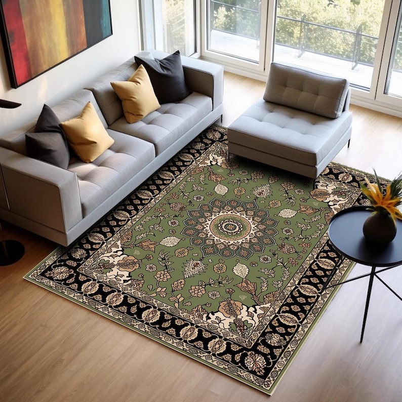 a modern living room with a gray sofa, a white ottoman, and a large green area rug with a floral pattern. The room is well-lit, with large windows providing natural light. There is also a small table with a vase of flowers, adding a touch of elegance to the space.