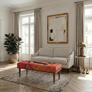 Op de afbeelding: Woonkamer met een bank met een rood en oranje patroon, geplaatst voor een lichtgekleurde bank. De kamer omvat een groot abstract kunstwerk, een plant in een pot en een bijzettafel met een lamp.