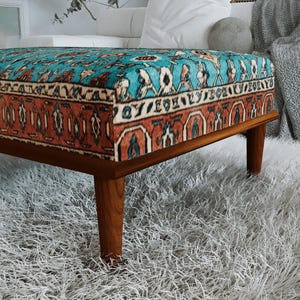 a modern, wooden ottoman with a vibrant, patterned cushion on top, placed on a fluffy white rug.