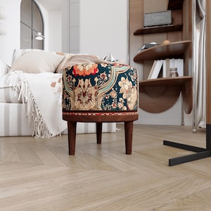 May include: A round ottoman featuring a dark teal fabric upholstery with a vibrant floral and paisley pattern in shades of orange, gold, and cream. The piece is supported by three tapered wooden legs with a rich brown finish and a matching wood base.
