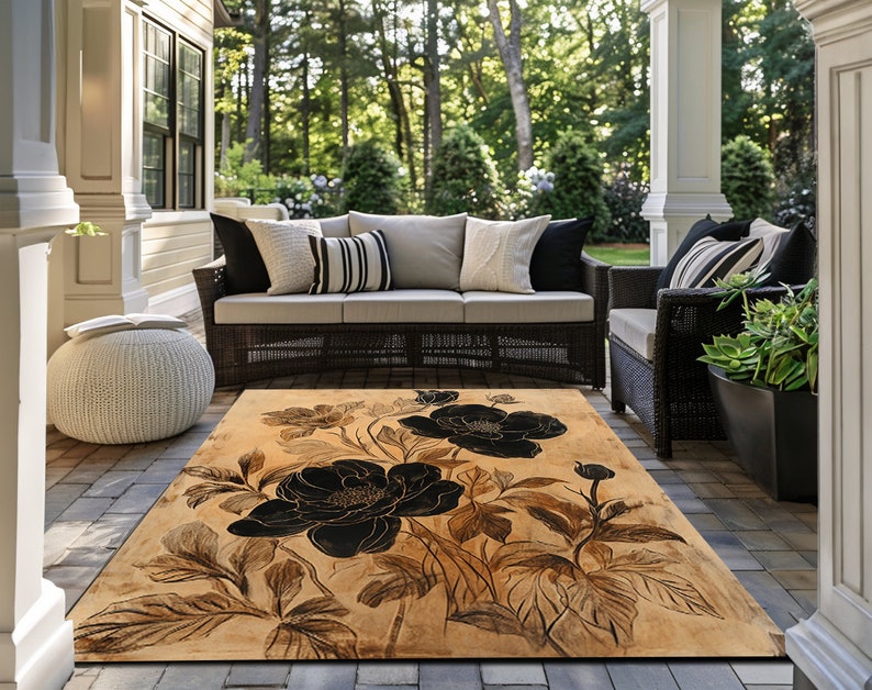 May include: A beige and black floral area rug with a large black flower design. The rug is on a patio with wicker furniture.