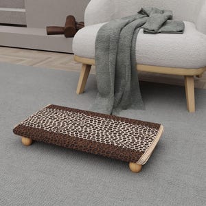 May include: A rectangular footstool with a leopard print design. The stool has a brown border and is supported by four small, rounded wooden legs. The top surface features a pattern of tan spots on a cream background.
