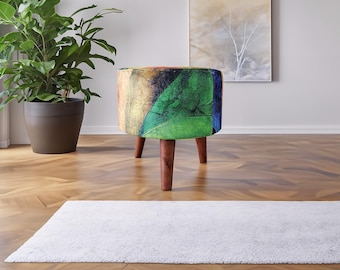 May include: A round ottoman featuring a vibrant, multi-coloured abstract pattern with prominent shades of green, yellow, and blue. The piece is supported by three tapered, dark brown wooden legs that provide a stable base for the circular seat.