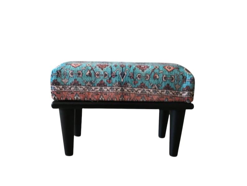 A colorful ottoman with a patterned design sits on a black wooden stand against a white background.
