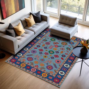 May include: A rectangular area rug with a light blue background and a border of dark blue, red, and yellow. The rug features a repeating pattern of colorful floral and geometric designs. The rug is placed on a hardwood floor in a living room setting.