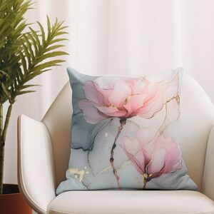 May include: A decorative throw pillow with a watercolor-style design featuring two pink flowers with gold accents on a light blue background.