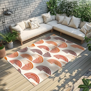 May include: A white area rug with a geometric pattern of orange and brown semi-circles. The rug is on a wooden floor in a patio setting with a white couch in the background.