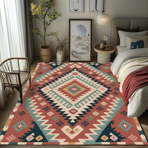 Puede incluir: Una alfombra colorida con un patrón geométrico en tonos de rojo, turquesa, crema y azul marino. La alfombra presenta un diseño central de diamante y un borde en zigzag, adecuada para un dormitorio o sala de estar.