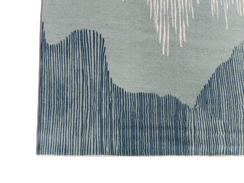 May include: Close-up of a blue and white patterned rug with a textured surface. The rug has a geometric design with vertical lines and wavy shapes.