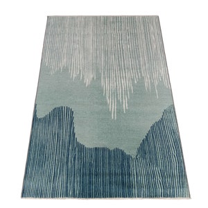 May include: Abstract area rug with a blue and white striped pattern. The rug has a light blue background with white stripes and a darker blue border with white stripes.