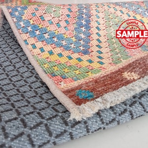 May include: A colorful rug with a geometric pattern. The rug has a fringe border and is folded in half. The rug is labeled "SAMPLE" in red.