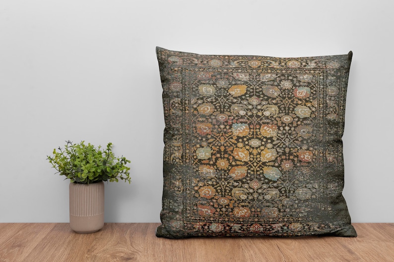 K&ouml;nnte beinhalten: Quadratisches Zierkissen mit einem detaillierten Blumenmuster in Gold, Orange und Blau auf dunklem Hintergrund. Das Kissen hat einen Vintage-Look. Es liegt auf einer Holzoberfl&auml;che.