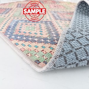 May include: A close-up of a colorful patterned rug with a gray non-slip backing. The rug has a white border and a geometric design with pink, blue, green, and yellow colors.