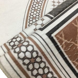 a close-up view of a patterned fabric, possibly a rug or textile, with a repeating geometric design in shades of brown and white.