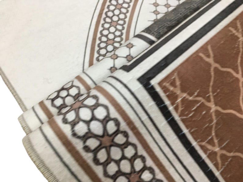 a close-up view of a patterned fabric, possibly a rug or textile, with a repeating geometric design in shades of brown and white.