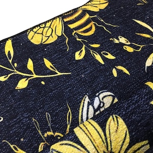 a close-up view of a fabric with a floral pattern in shades of yellow and black. The fabric appears to be a dark-colored material with a textured surface.