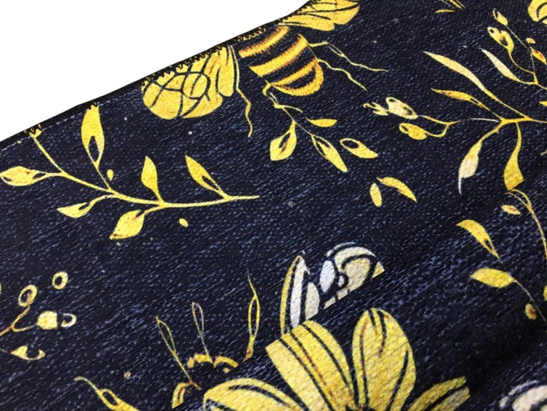 a close-up view of a fabric with a floral pattern in shades of yellow and black. The fabric appears to be a dark-colored material with a textured surface.
