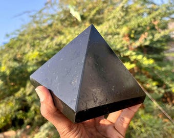 May include: A black obsidian pyramid crystal, a geometric shape with four triangular sides and a square base. The crystal is smooth and polished, with a dark, reflective surface.