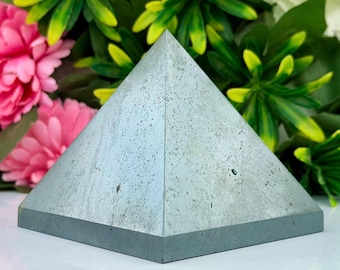 May include: A pyramid-shaped object made of a smooth, light gray concrete material with a speckled, porous texture. The base is square, and the four triangular faces meet at a sharp apex, showcasing a solid, geometric form and matte finish.