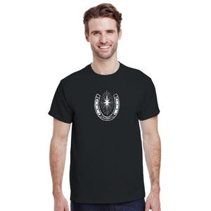 May include: A black short-sleeved t-shirt featuring a white graphic print on the chest. The design depicts a horseshoe positioned vertically with a radiant starburst element centred within the arch, rendered in a detailed line art style.