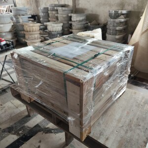 K&ouml;nnte beinhalten: Ein gro&szlig;er Holzkasten, der in durchsichtige Plastikfolie verpackt ist, mit gr&uuml;nen Gurten gesichert und auf einer Holzpalette steht. Der Kasten befindet sich in einem Lagerhaus mit anderen Kisten und Boxen im Hintergrund.