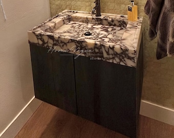 Op de afbeelding: Een zwevend badkamermeubel met een donkergrijze kast met twee deuren en een wit marmeren blad met opvallende zwarte aders. Een zwarte kraan is in het midden van de wastafel geplaatst en de tekst Home Vogue Designs is zichtbaar.