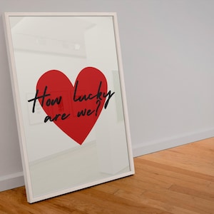 Op de afbeelding: Een witte ingelijste print met een rood hart en de tekst "How lucky are we?" in zwart.