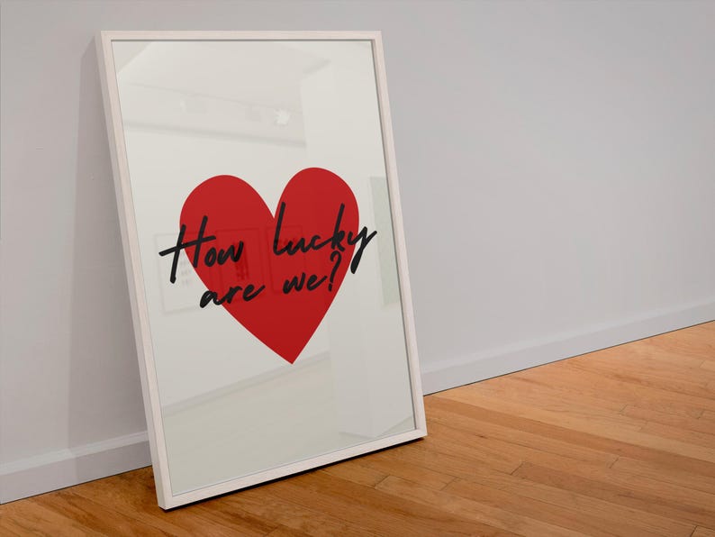 Op de afbeelding: Een witte ingelijste print met een rood hart en de tekst "How lucky are we?" in zwart.