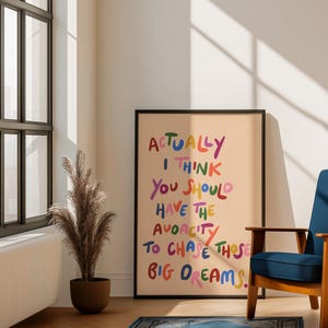 Peut inclure: Une affiche encadrée avec le texte "ACTUALLY I THINK YOU SHOULD HAVE THE AUDACITY TO CHASE THOSE BIG DREAMS" en lettres colorées. L'affiche est exposée dans une pièce avec une chaise bleue, un tapis et une plante en pot.