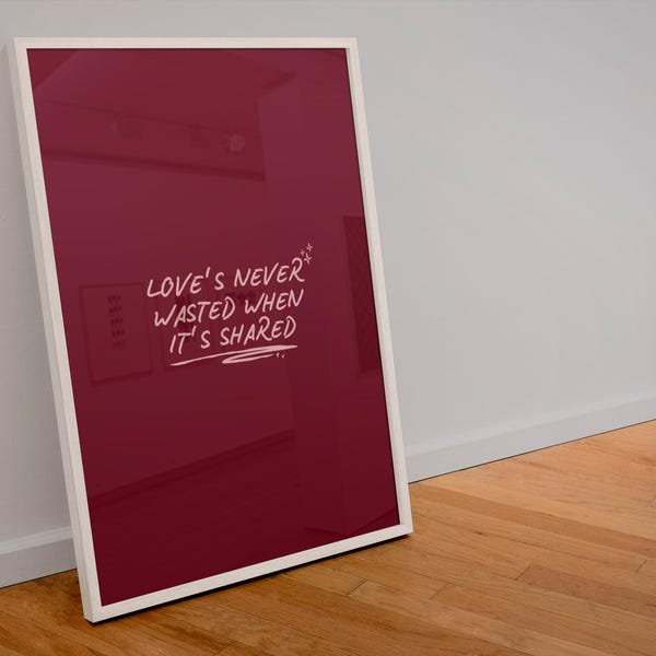 Könnte beinhalten: Ein gerahmter Kunstdruck mit weißem Rand, der an einer Wand lehnt. Der Druck hat einen tiefroten Hintergrund mit dem handgeschriebenen Text "LOVE'S NEVER WASTED WHEN IT'S SHARED" in Weiß. Das Kunstwerk wird auf einem Holzboden ausgestellt.