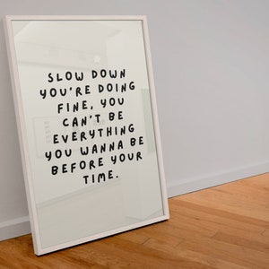 May include: White framed print with the text "Slow down you're doing fine, you can't be everything you wanna be before your time."