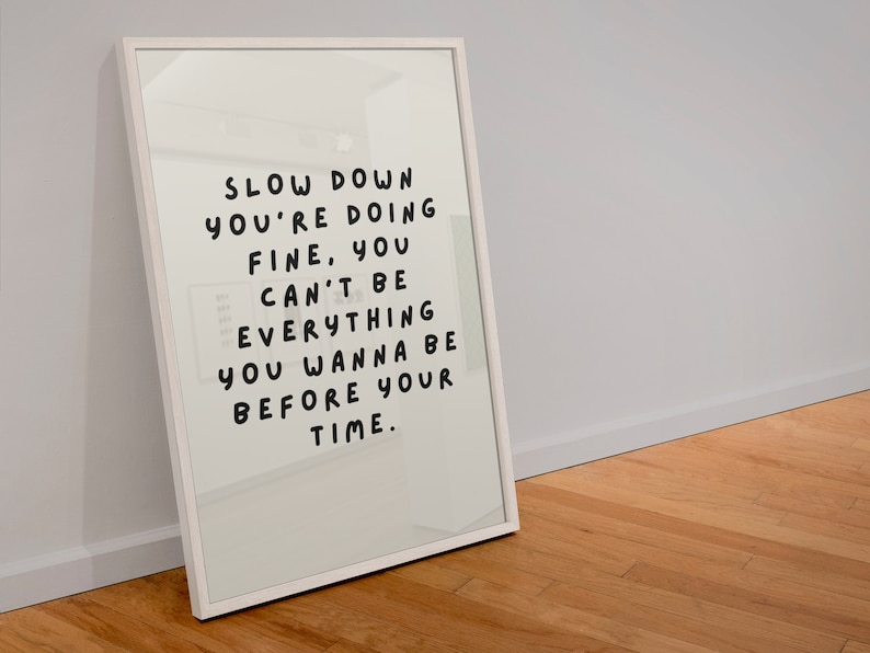 May include: White framed print with the text "Slow down you're doing fine, you can't be everything you wanna be before your time."