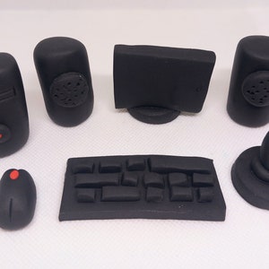 May include: A set of black computer accessories, including a monitor, keyboard, mouse, speakers, and a joystick. The mouse and joystick have red accents. The items are arranged on a white surface.