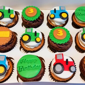 Pode incluir: Uma dúzia de cupcakes numa caixa branca, cada um decorado com desenhos de tratores em verde, azul e vermelho, e alguns com o número 3 ou "Happy Birthday". Os cupcakes têm cobertura branca e bolo de chocolate.