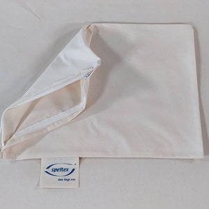 May include: A white pillowcase with a zipper closure. The pillowcase is made of a soft, natural fabric. The brand name "speltex" is printed on a blue label attached to the pillowcase.