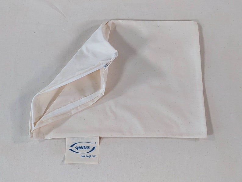 May include: A white pillowcase with a zipper closure. The pillowcase is made of a soft, natural fabric. The brand name "speltex" is printed on a blue label attached to the pillowcase.