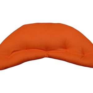 Könnte beinhalten: Ein halbmondförmiges Meditationskissen aus einfarbigem, leuchtend orangefarbenem Stoff. Das Kissen hat eine glatte, abgerundete Oberkante und eine leicht geschwungene Unterseite mit zwei symmetrisch angeordneten, gesteppten Vertiefungen.