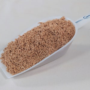 Könnte beinhalten: Eine weiße Schaufel gefüllt mit hellbraunem Quinoa.