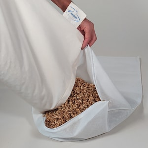 Puede incluir: Una funda de almohada blanca se está vaciando, revelando una almohada blanca llena de cáscaras de trigo sarraceno marrones.