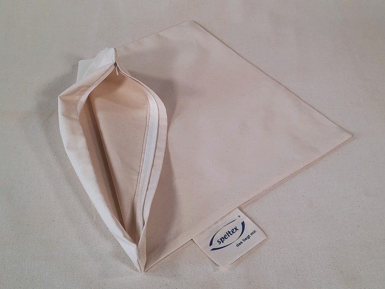 May include: A beige pillowcase with a zipper opening. The pillowcase has a white label with the text "spelltex das liegt mir."