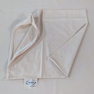May include: A white pillowcase with a zipper closure. The pillowcase is folded in half and the zipper is open. The pillowcase has a blue label with the text "spertex das liegt mir" on it.