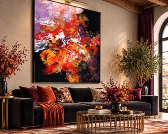 Puede incluir: Una gran pintura abstracta cuadrada con vibrantes salpicaduras de pintura roja, naranja, morada y blanca sobre un fondo negro intenso, exhibida en un marco sobre un sofá oscuro en una sala de estar con iluminación cálida.