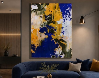 May include: A large rectangular wall art piece featuring an abstract composition of bold yellow, deep blue, white, and dark green paint strokes. The artwork is framed in a thin gold border and hangs centered above a dark blue sectional sofa.