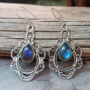 May include: Silver dangle earrings with a teardrop-shaped blue labradorite gemstone set in a filigree design.