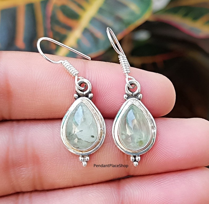 May include: A pair of silver teardrop earrings with green gemstone accents. The earrings have a delicate design and are perfect for everyday wear.