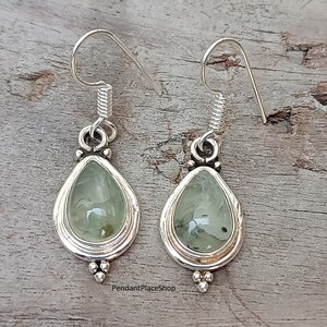 May include: A pair of silver dangle earrings with green gemstone drops. The earrings have a teardrop shape and are accented with small silver beads.