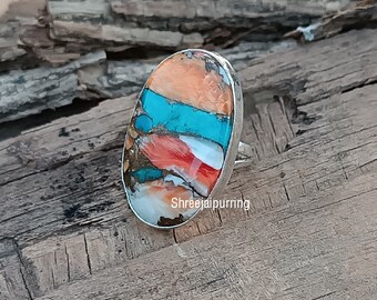 May include: A silver ring with an oval shaped turquoise and coral stone. The stone has a layered pattern of turquoise, coral, and white.