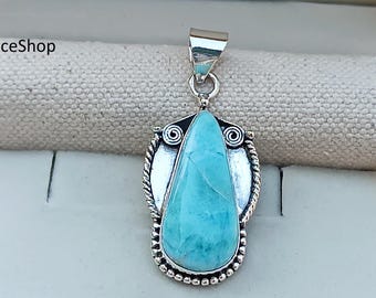 May include: A silver pendant featuring a teardrop-shaped, light blue gemstone. The gemstone is set in a decorative silver frame with a rope-like border and spiral accents. The pendant has a silver bail for attaching to a chain.